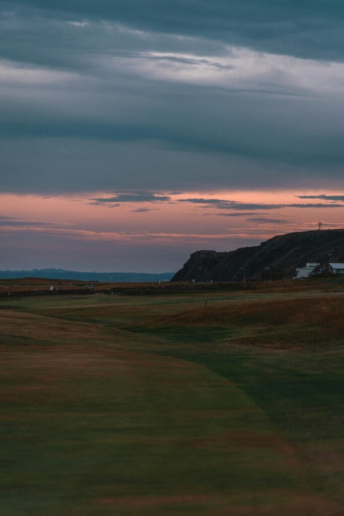 A dramatic twilight sky with orange and purple clouds over a rolling green Highland landscape and distant cliffs at twighlight.